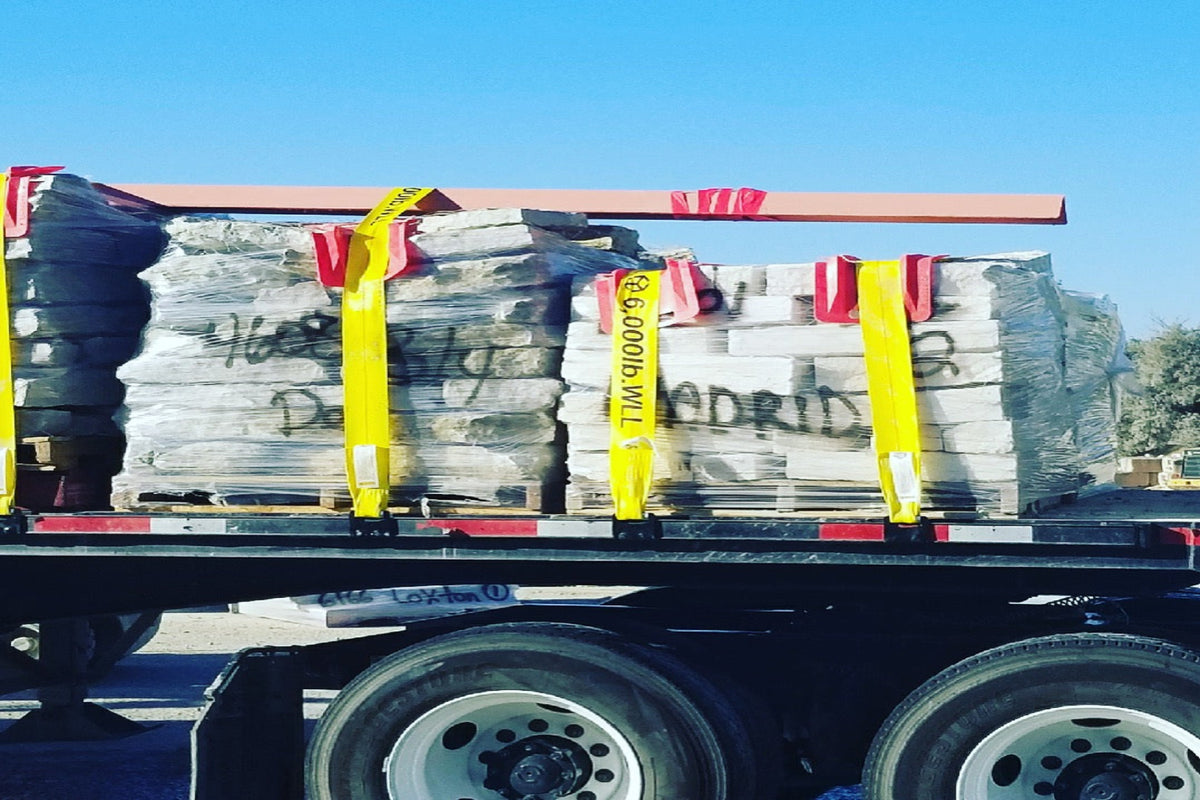 Stacked freight strapped down with yellow ratchet straps on a flatbed truck.