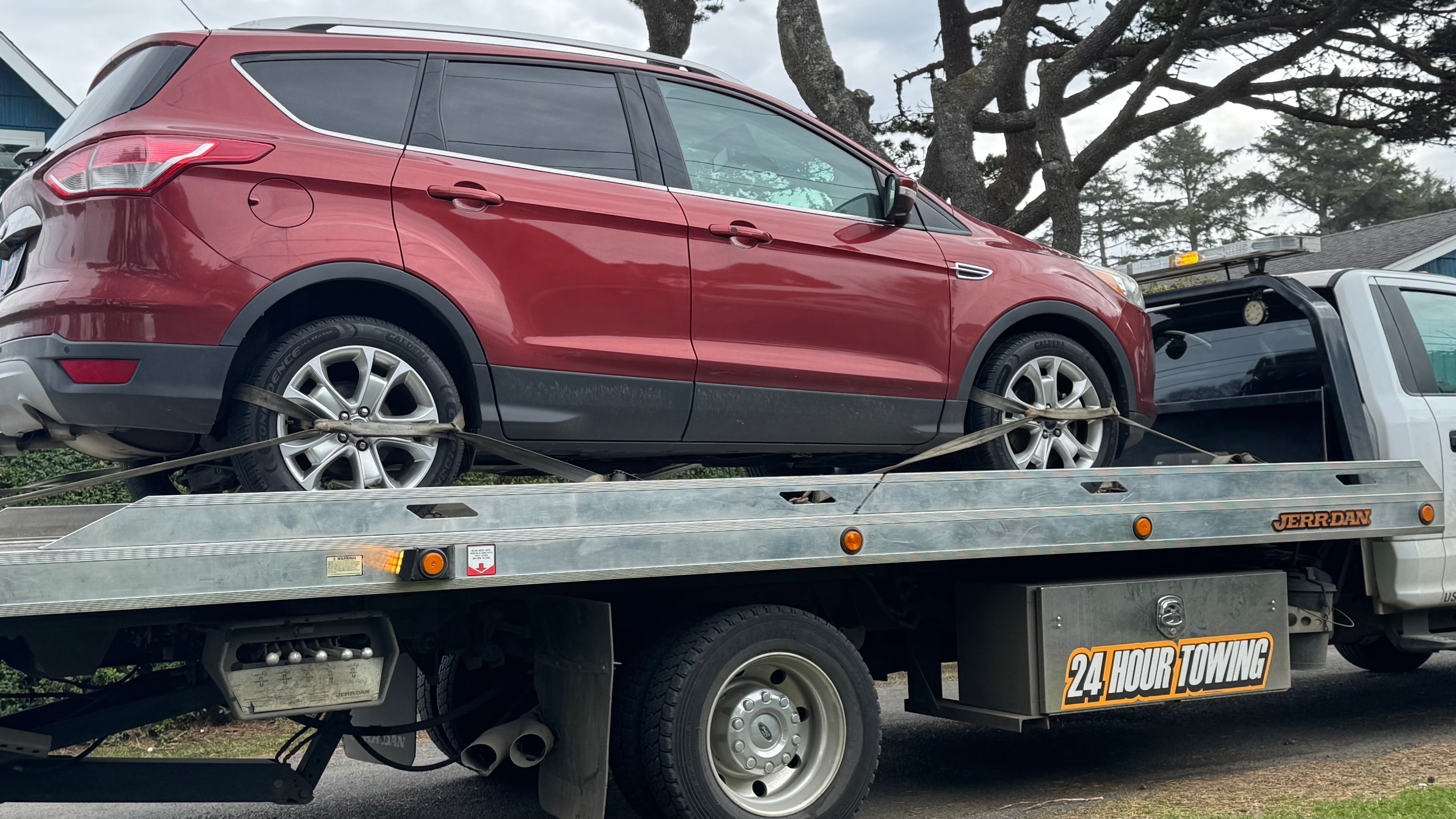 Red SUV secured on the bed of a rollback tow truck.