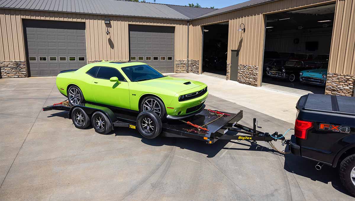 Sports car loaded on an open car hauler trailer behind a pickup truck.